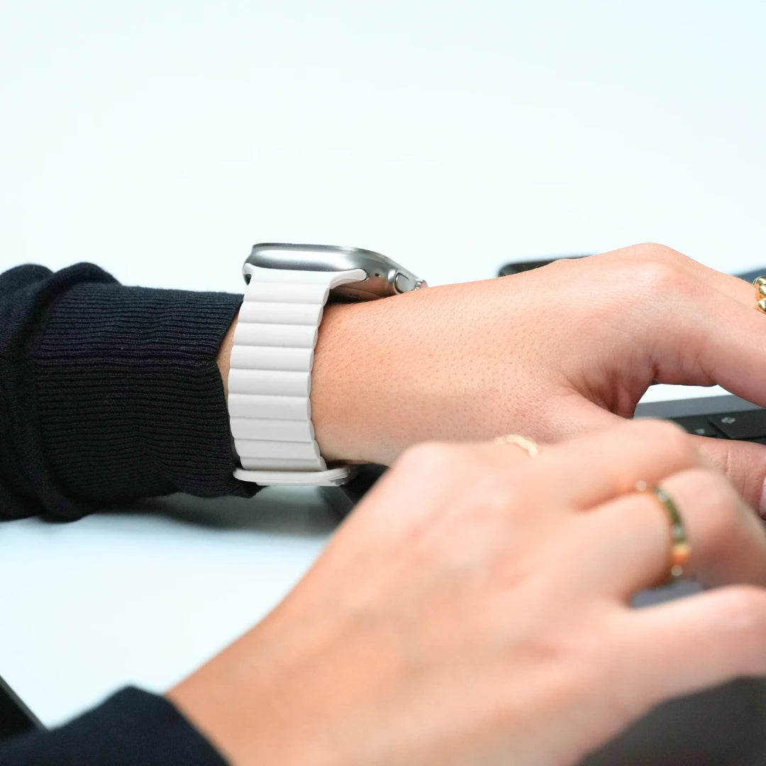 Apple Watch mit weißem Gliederarmband aus Silikon – modernes Design am Handgelenk während der Arbeit am Schreibtisch.