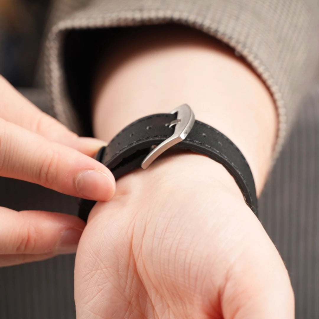Nahaufnahme des silbernen Dornverschlusses am schwarzen Lederarmband, das ums Handgelenk gelegt wird. #farbe_schwarz