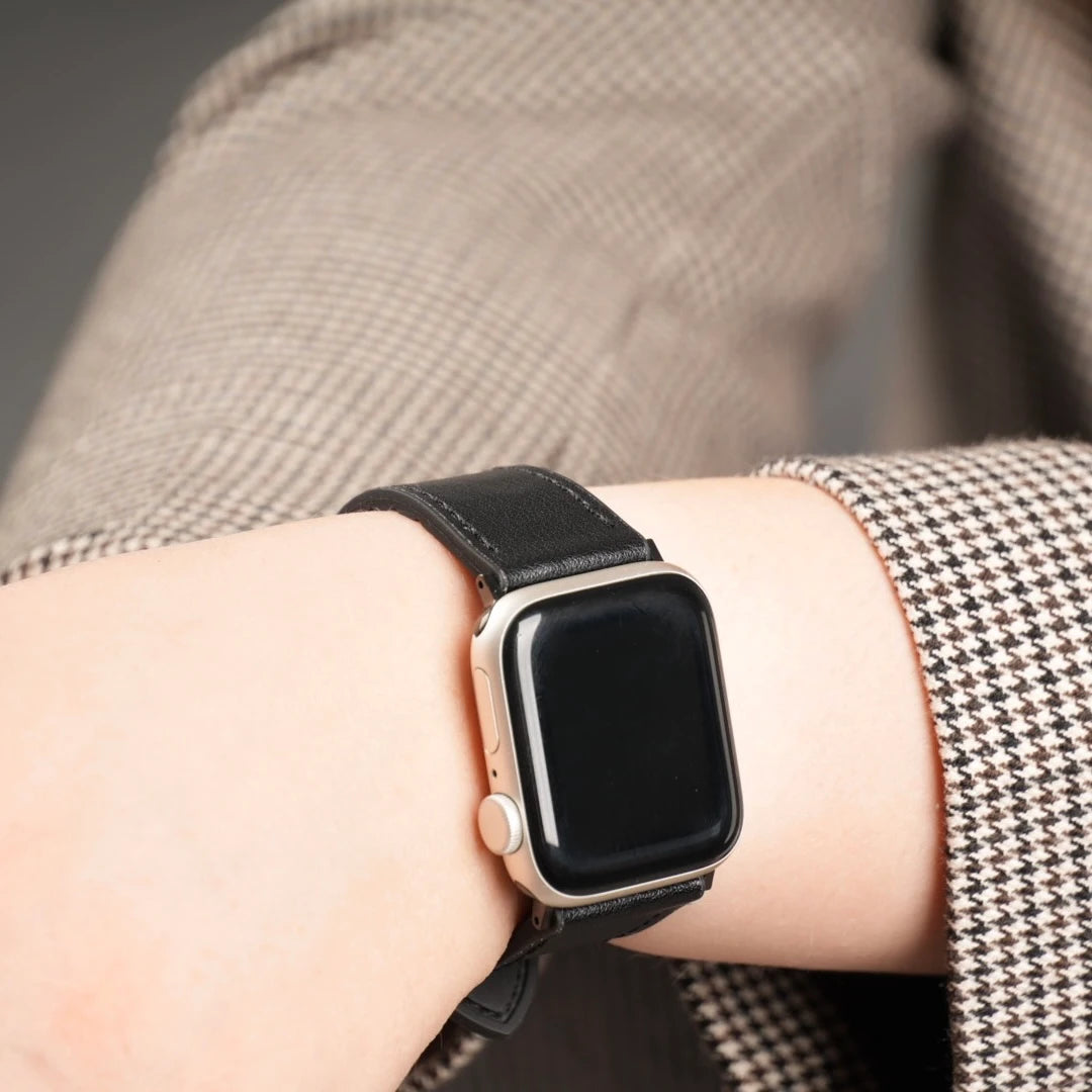 Apple Watch mit schwarzem Lederarmband seitlich getragen, stilvoll kombiniert mit kariertem Blazer. #farbe_schwarz