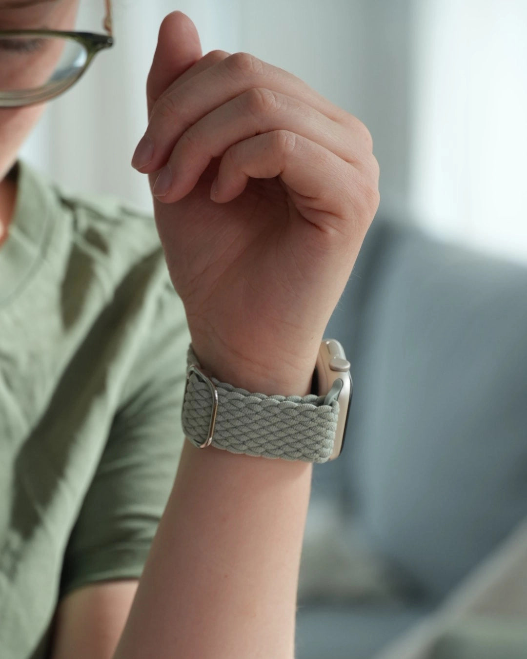 Nahaufnahme eines hellgrünen geflochtenen Apple Watch Armbands am Handgelenk einer Person mit Brille und grünem T-Shirt
