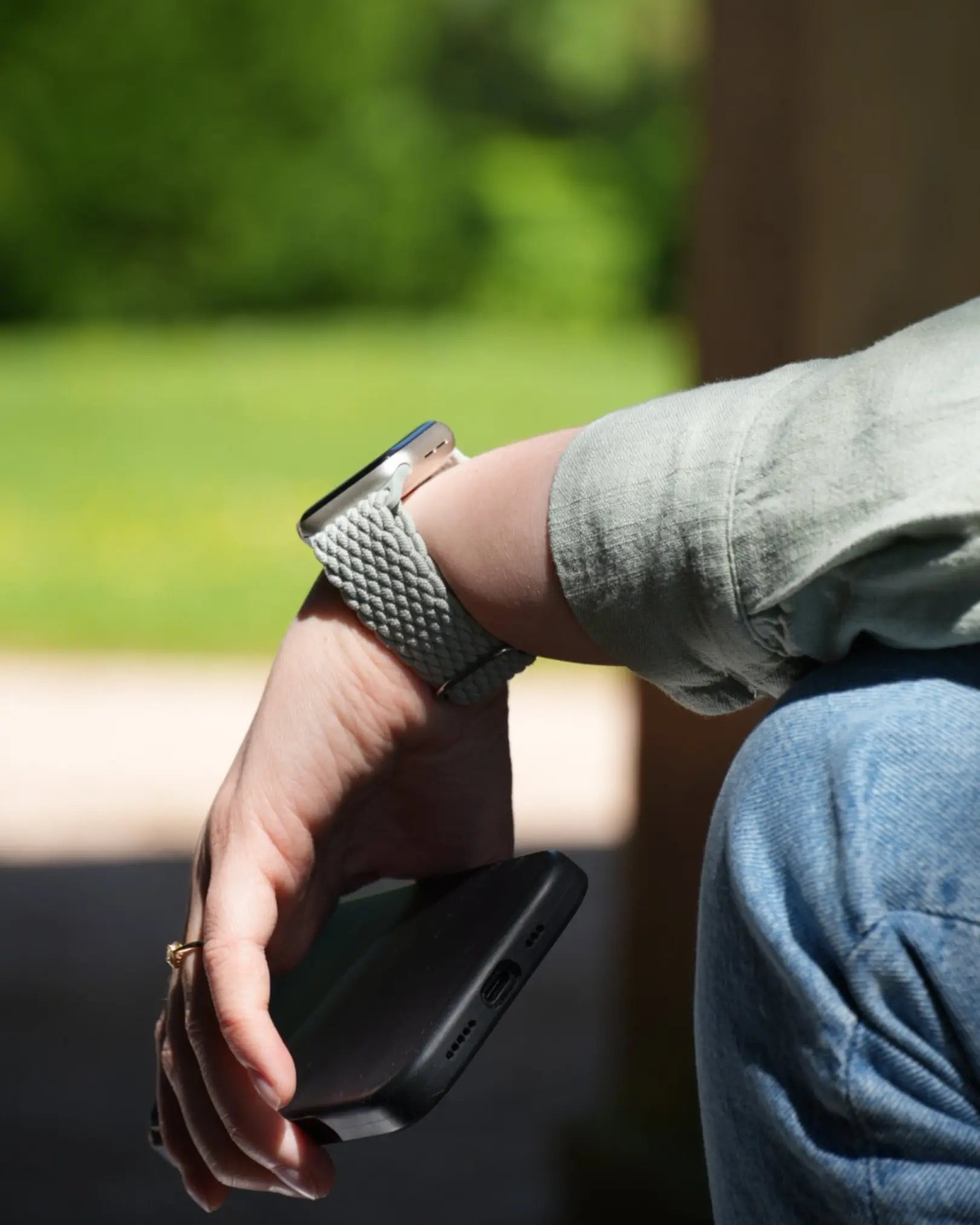 Apple Watch mit gewebtem Armband in Hellgrün am Handgelenk, im Freien mit Smartphone in der Hand